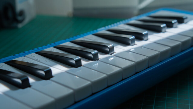 a closeup shot shows the white and black keys of a blue melodica resting on a green gridded cutting mat, angled slightly.