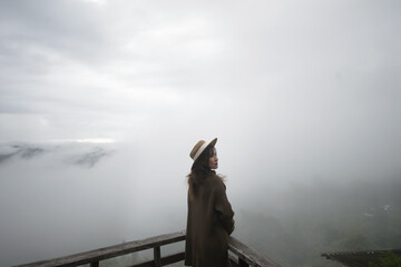 Fototapeta premium A woman stands on a wooden deck, gazing into a foggy landscape, enveloped by clouds and nature