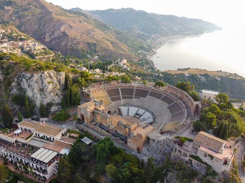 Aerial view of the ancient Teatro Greco ruins standing in stark contrast to the azure sea and rolling hills, a timeless tableau of history and nature, Taormina, Sicilia, Italy.