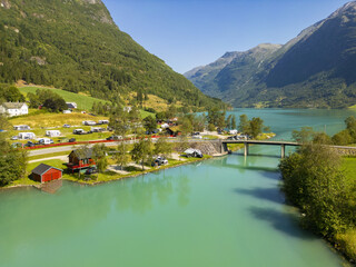 Aerial view of turquoise waters of Oldevatnet reflecting the bright sky, a bridge connecting the shores near a camping site nestled at the foot of towering mountains, Oldevatnet, Vestland, Norway.
