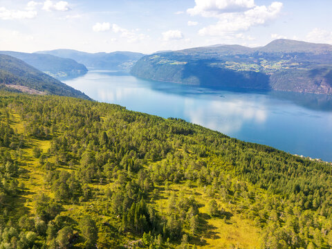 Aerial view of the serene fjord cutting through the verdant hills under a vast sky, creating a tapestry of blues and greens, Utvik, Vestland, Norway.