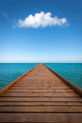 Fototapeta premium Wooden pier stretching into the ocean under a blue sky with a single cloud