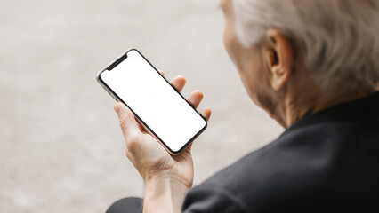 A pair of hands, belonging to an elderly person, holds a smartphone with a blank screen. Ideal for themes of senior citizens and technology, digital literacy, and user-friendly interfaces.