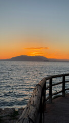 Fototapeta premium Malaga, Spain. Sunset on the Rincon de la Victoria, Malaga with views of the mountain El Monte Calamorro. Scenic sunset view over ocean with wooden railing and distant mountains in the background