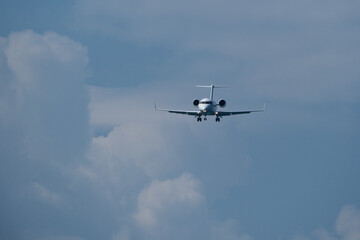 Airplane in the blue sky with white clouds and landing gear. The private plane is preparing to land at the airport on a sunny day.