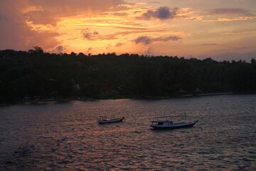 Naklejka premium Small fishing boats floating on calm sea with warm sunset sky, perfect for travel editorials, tourism ads, and peaceful coastal scene designs