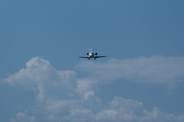 Airplane in the blue sky with white clouds and landing gear. The private plane is preparing to land at the airport on a sunny day.