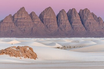 Pink-hued mountain range behind a vast expanse of white sand dunes
