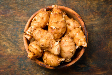 Organic fresh Jerusalem Artichokes or sunroot in a wooden bowl. Top view.