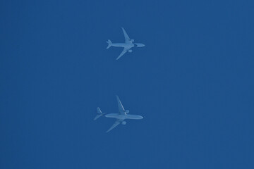 Two airplanes are flying in a clear blue sky on parallel courses.