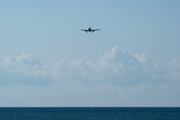 Airplane flying in the blue sky over the sea with white clouds. Airplane in the blue sky with white clouds above the sea.
