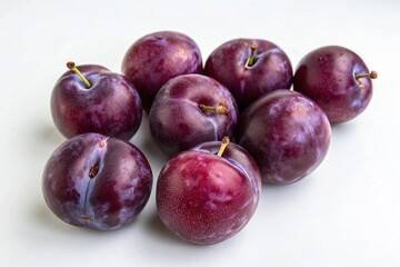 Fototapeta premium Fresh ripe plums arranged on a white surface on white background