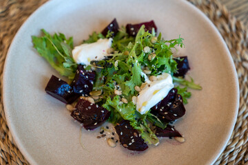 Beetroot salad with greens, mozzarella, and seeds on a ceramic plate
