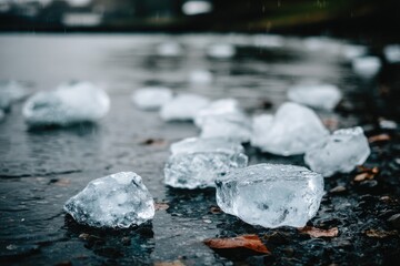 Ice cubes scattered on wet dark ground by a body of water