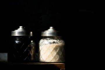 Glass spice jars with metal lids photographed in low key lighting, highlighting texture and form. Perfect for kitchen, cooking, and rustic food styling concepts.