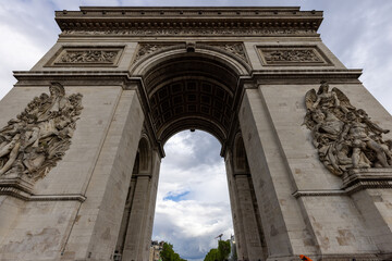 View of the imposing Arc de Triomphe, a monumental arch sculpted with intricate details against the backdrop of a cloudy sky, Paris, ÃŽle-de-France, France.