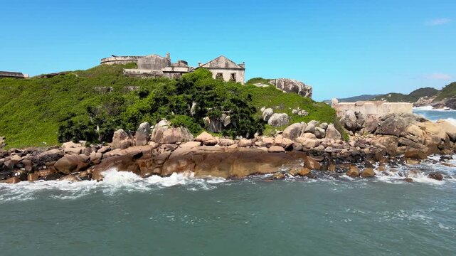 Orbital aerial drone scene of an ancient 18th century ruined fortress on a small isolated rocky island imperial defense system, Florian&oacute;polis, Santa Catarina, Brazil, Ara&ccedil;atuba, Naufragados beach