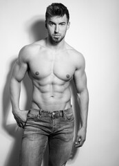 Naklejka premium Athletic and fit bodybuilder posing shirtless in jeans flexing muscles after workout showing off six-pack