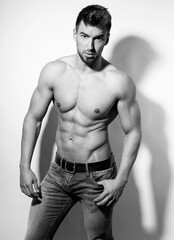 Naklejka premium Athletic and fit bodybuilder posing shirtless in jeans flexing muscles after workout showing off six-pack