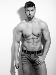 Fototapeta premium Athletic and fit bodybuilder posing shirtless in jeans flexing muscles after workout showing off six-pack