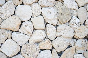 A close-up view of an old stone wall made of irregularly shaped, light-colored rocks tightly fitted together