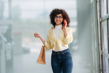Conversation by using phone. Beautiful woman is standing indoors against blurred wall
