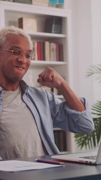African American man sits at his laptop, receives an exciting email, waves his hands with pure joy, and celebrates the new opportunities that promise a brighter future ahead.