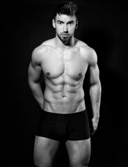 Fototapeta premium Handsome bodybuilding man posing shirtless on black background flexing muscles and six pack after a workout