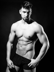 Fototapeta premium Handsome young muscular bodybuilding man posing in underwear with visible six pack in black and white