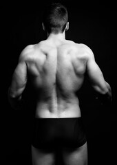 Fototapeta premium Handsome bodybuilding man posing shirtless on black background flexing muscles and six pack after a workout