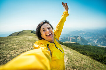 Senior woman with backpack taking selfie on top of the mountain - Smiling aged female hiking outside - Sport and technology life style concept