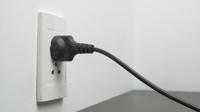 Female hand inserting a black electrical plug into outlet