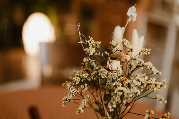 spring dried flowers in a vase, floral decoration art in a warm tone background, wooden table and bright yellow light in the back