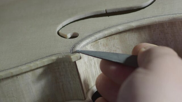 Skilled luthier carefully carving violin's f hole edges with specialized gouge, revealing intricate craftsmanship behind creating fine musical instrument