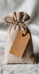 Small burlap sack tied with twine, featuring a blank brown tag, rests on a light-colored fabric