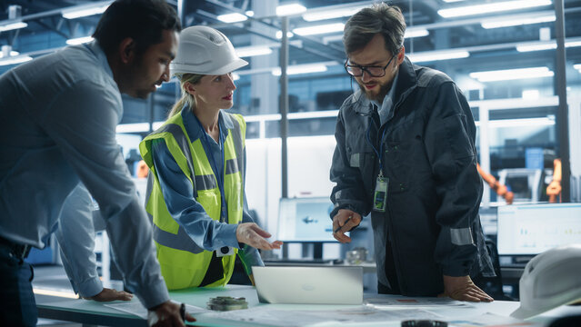 Young Diverse Team of Industrial Engineers Working in Office at Factory. Female Professional Technician Talks About Electric Engine Production. Autonomous Production Facility With Robotic Hands.