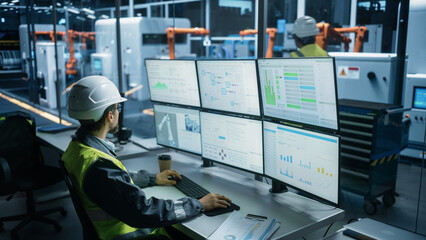 Caucasian Male Process Engineer Using Multi Monitor Workstation To Control Production Of Modern Heavy Machinery on Autonomous Assembly Line With Robotic Arms. Man Adjusting Manufacturing Processes.