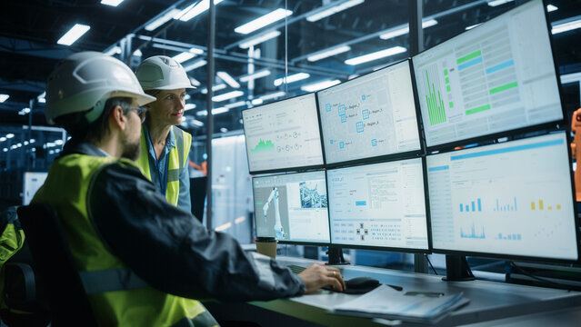 Caucasian Male Process Engineer Using Multi Monitor Workstation And Talking To Female Production Supervisor At Electronics Factory. Colleagues Monitoring Autonomous Assembly Line With Robotic Arms - Powered by Adobe