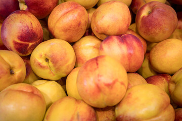 A vibrant, close-up background of fresh, ripe nectarines piled together at a market. A colorful and juicy image representing summer fruits, healthy eating, vitamins, and natural, organic produce.