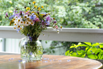 Bouquet of wild flowers in a glass vase on a wooden table