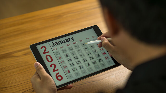 January 2026 new year calendar on digital tablet, person scheduling plans and strategies for business growth and future success, focusing on goal setting and productivity.