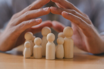 Protection and care concept with human hands sheltering wooden figures, symbolizing family safety,...
