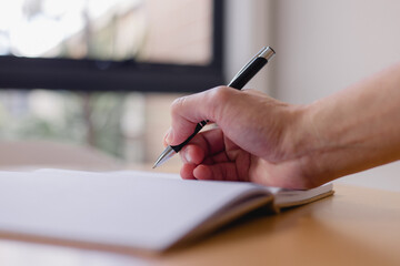 Writing and creativity concept with a close-up of a hand holding a pen and writing in a lined notebook, symbolizing note-taking, planning, education and personal or professional documentation.