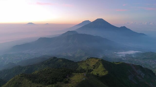 Peaceful sunrise aerial view of tropical mountain range with layers of hills and mountain summits. Amazing morning scenery from Mount Prau, Indonesia. Tropical nature landscape.