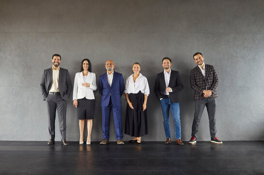 Full length shot of six busness people dressed formally, ready for corporate meeting, isolated over grey studio wall. Full body portrait of team of corporate workers posing indoor.