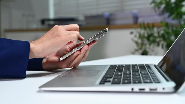 Closeup of hands multitasking with smartphone and laptop in a bright office. Concept of remote work, digital communication