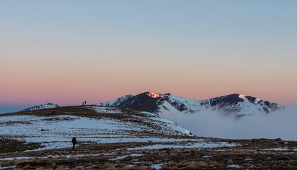 Solitary hiker witnessing a breathtaking sunset over a snow-covered mountain range from a high-altitude plateau.