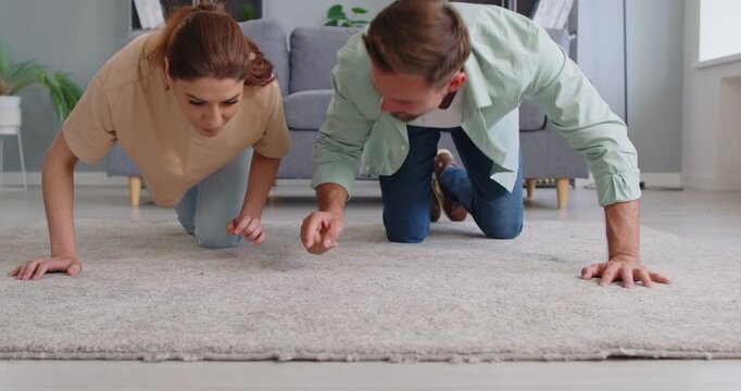 Man and woman crawling on the living room floor while searching for a lost item on the carpet. Focused facial expressions and body posture suggest urgency or frustration. 