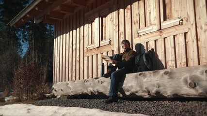 Man in hiking wear and boots with backpack sitting on bench in forest with map