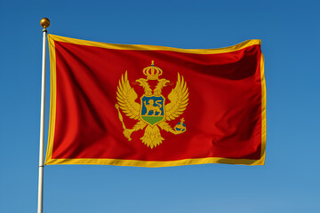 Montenegro flag waving with golden eagle emblem against a blue sky.